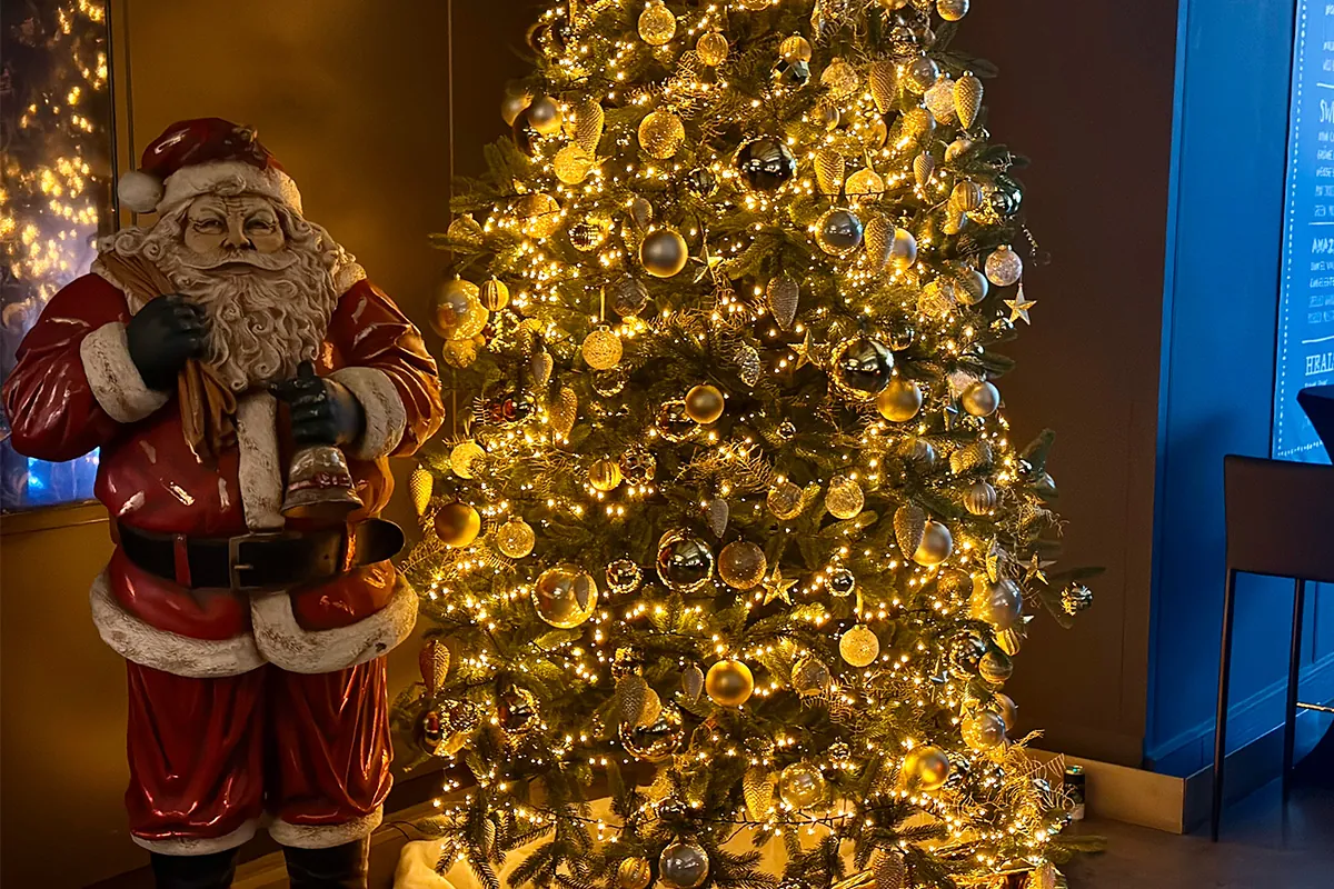 Weihnachtsmann-Figur neben einem goldenen Lichterbaum